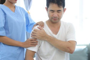 Doctor diagnosing man's shoulder pain in hospital examination room.